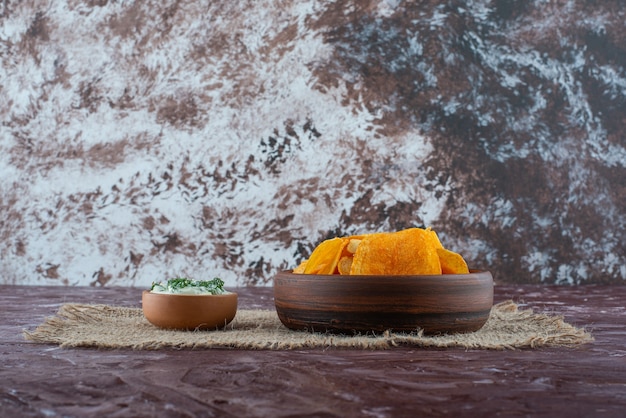Batata frita crocante e iogurte em pratos na textura, na mesa de mármore.