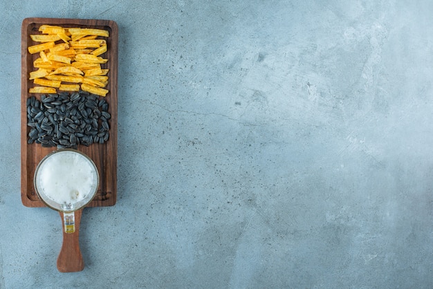 Batata frita, sementes de girassol e um copo de cerveja em uma placa, sobre o fundo azul.