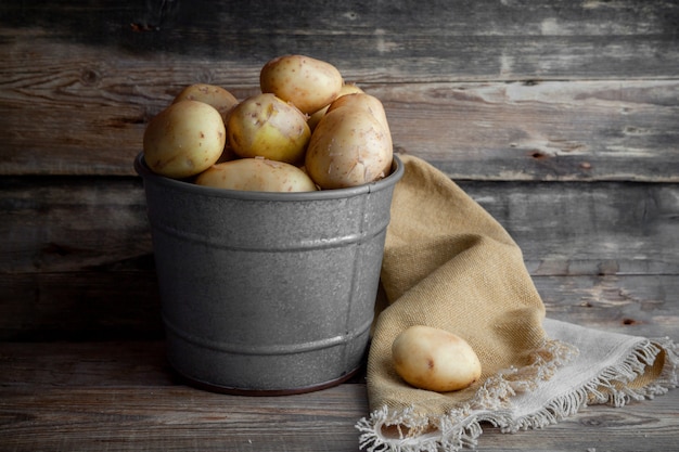Batatas da vista lateral no balde cinza no fundo escuro de madeira. horizontal