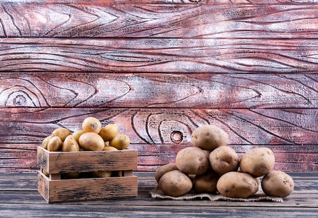 Batatas em uma caixa de madeira e no saco saco vista lateral em uma mesa de madeira