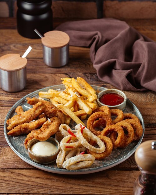 Batatas fritas com asas de frango frito e anéis de cebola com ketchup na mesa de madeira marrom