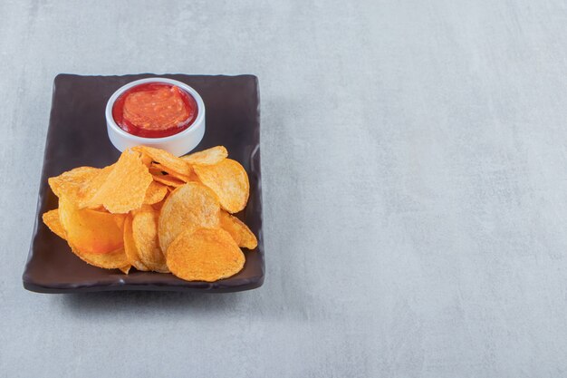 Batatas fritas com especiarias saborosas e ketchup colocados em um prato escuro.