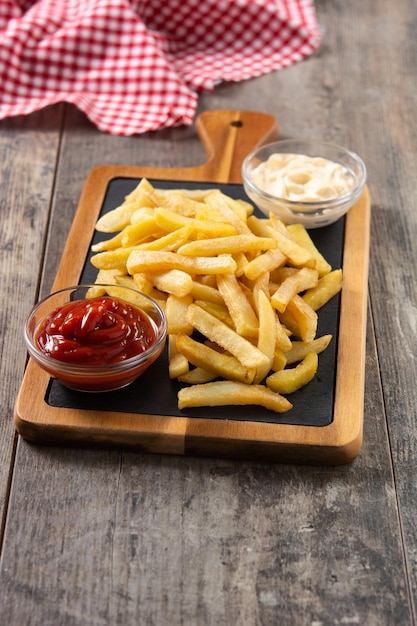 Batatas fritas com ketchup e maionese na mesa de madeira