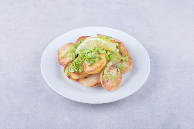 Batatas fritas decoradas com limão na chapa branca.