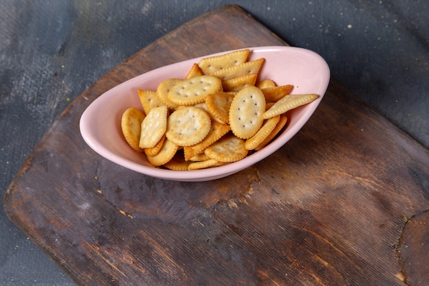 Batatas fritas e biscoitos de cima dentro da placa rosa na mesa de madeira e na foto do lanche de biscoito crocante de fundo cinza