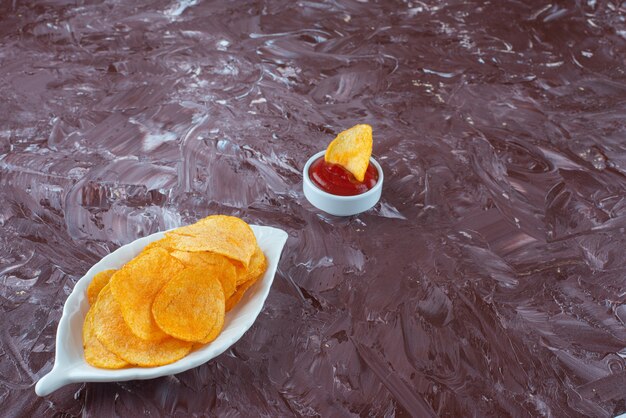 Batatas fritas em um prato ao lado do ketchup em uma tigela, na mesa de mármore.