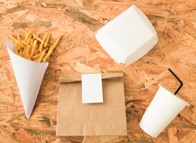 Batatas fritas no cone de papel e maquete de pacote em pano de fundo de madeira