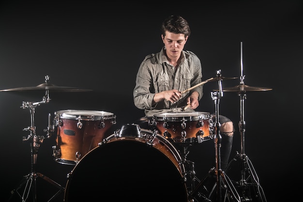 Baterista profissional tocando bateria no palco sobre o fundo preto com baquetas e look vintage. Vista do topo. Efeito de fumaça