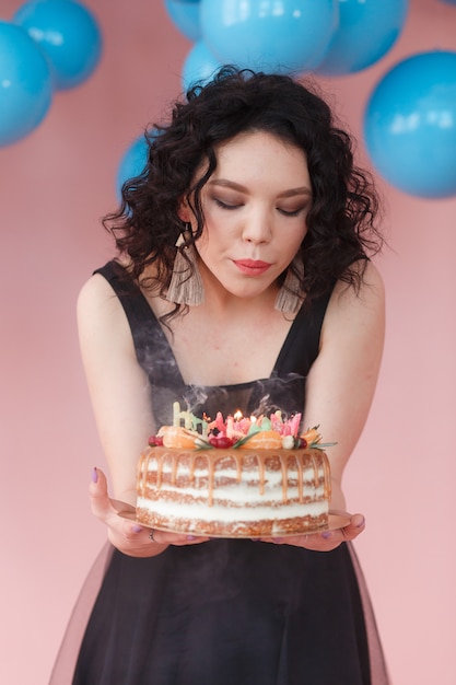 Foto grátis bautiful caucasiano garota soprando velas no bolo de aniversário. balões azuis no fundo.