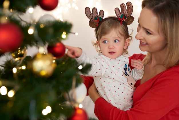 Bebê adorável e mamãe decorando árvore de Natal