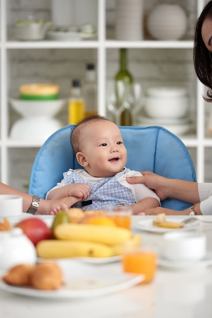 Bebê asiático bonito na mesa de jantar com a família