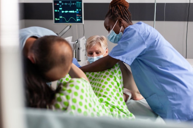 Foto grátis bebê de entrega de mulher na enfermaria do hospital, gritando e empurrando durante a cirurgia cesariana. equipe médica e futuro pai confortando gestante com contrações dolorosas na maternidade