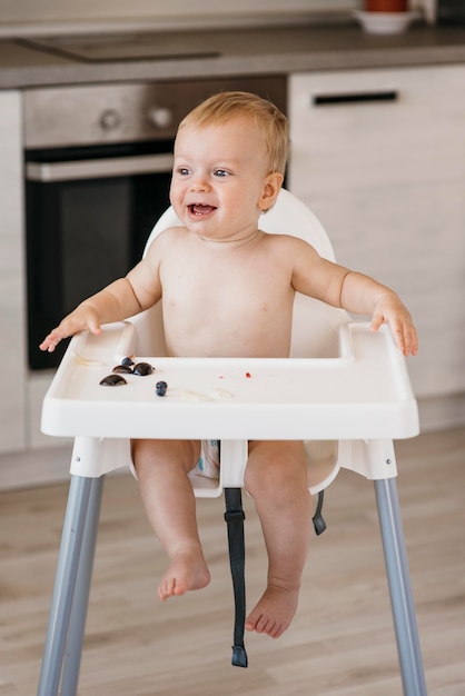 Bebé feliz na cadeira alta a escolher que fruta comer