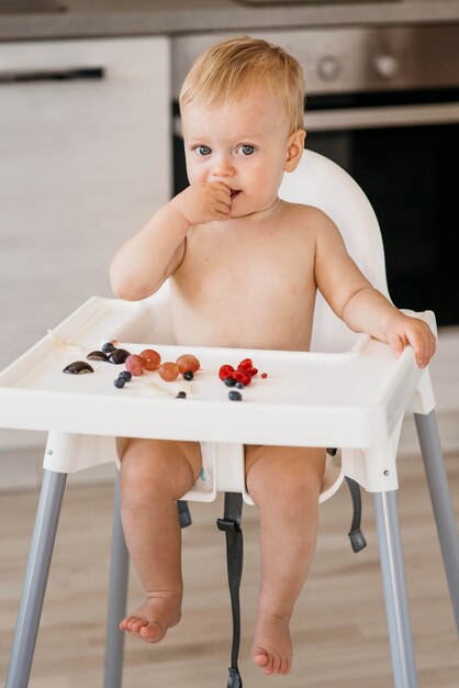 Bebê fofo em uma cadeira de bebê, de frente, escolhendo quais frutas comer