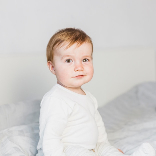 Bebê loiro bonito na cama branca