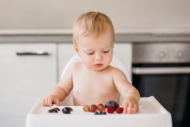 Bebé na cadeira alta a escolher que fruta comer