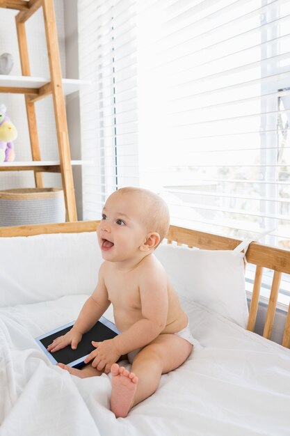 Bebé que joga com a tabuleta digital em um berço