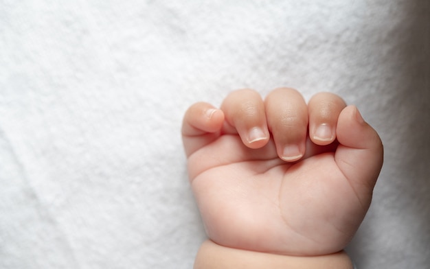 Bebê recém-nascido com a mão na cama branca