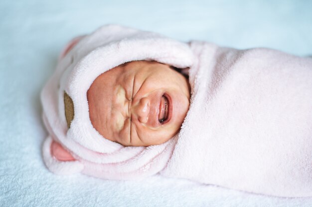 Bebê recém-nascido embrulhado em um cobertor rosa suave e chorando