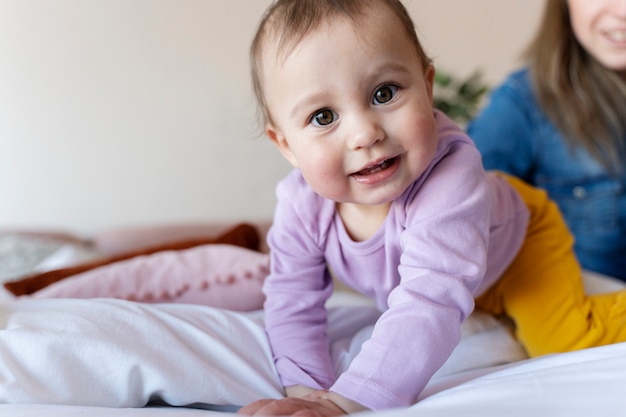 Bebê sorridente deitado na cama enquanto sua mãe está sentada ao lado dele