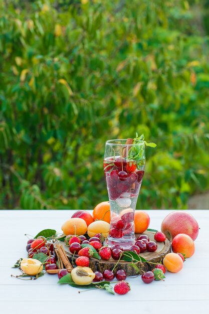 Beber com frutas, especiarias, tábua em um copo com fundo de madeira e jardim, vista lateral.