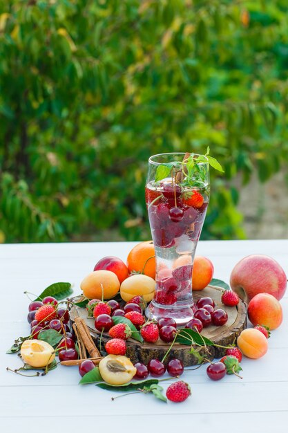 Beber com frutas, especiarias, tábua, folhas em um copo com fundo de madeira e jardim, vista lateral.