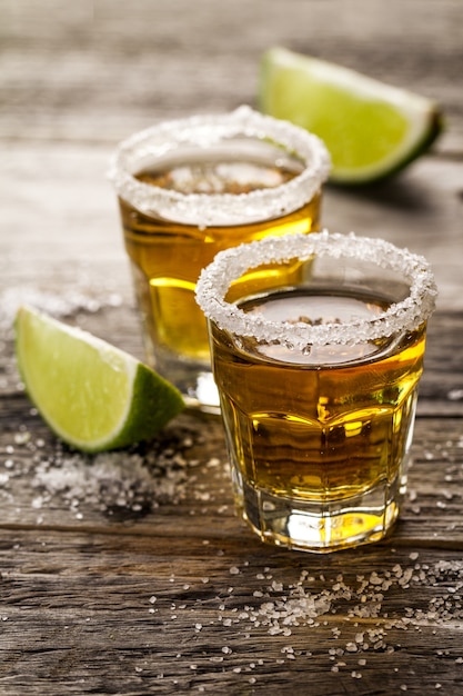 Bebida alcoólica saborosa com tequila com limão e sal no vibrante fundo de mesa de madeira. Fechar-se.