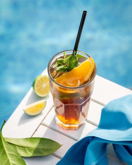 Bebida amarela com laranja, limão e hortelã folhas à beira da piscina.