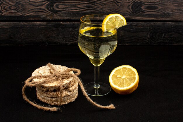 Bebida e biscoito bebida de limão com pedaços de limão dentro de vidro transparente, juntamente com biscoito de pão redondo em um rústico de madeira