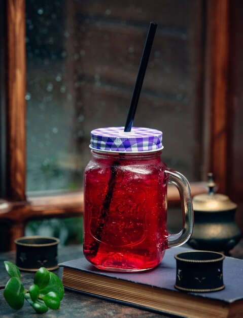 bebida rosa gelada em frasco de vidro com palha preta em frente à janela