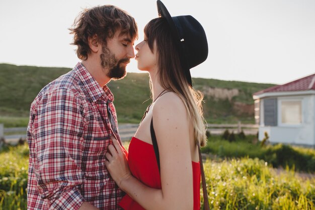 Beijo ensolarado abraçando um jovem casal elegante apaixonado no campo, estilo indie hippie boêmio, férias de fim de semana, roupa de verão, vestido vermelho