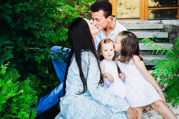 Beijos quentes de adoráveis ​​pais e suas filhas sentadas fora