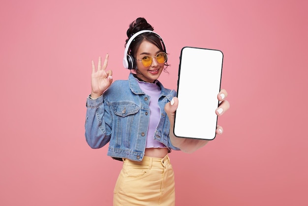 Bela adolescente asiática segurando um modelo de smartphone de tela em branco e mostrando o sinal ok