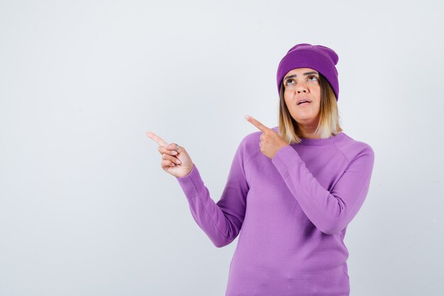 Bela dama apontando para o canto superior esquerdo de suéter, gorro e parecendo confiante. vista frontal.