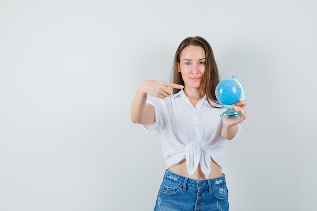 Bela dama de blusa branca, apontando para o mini globo, vista frontal. espaço para texto