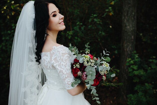 Bela e sorridente noiva segurando bouquet em pé lá fora