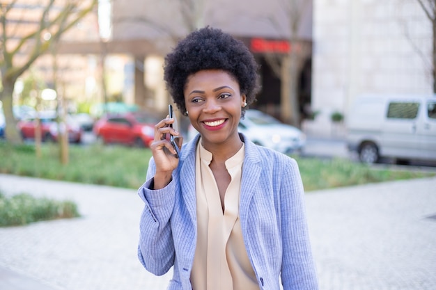 Bela empresária sorridente, falando no telefone na rua