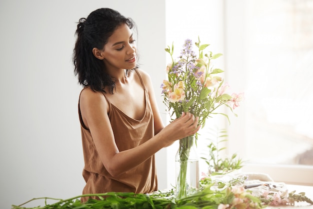 Bela florista feminina africana sorrindo fazendo buquê de flores.