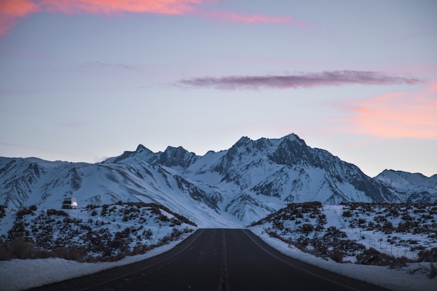 Bela foto ampla de uma estrada perto de montanhas cheias de neve sob um céu rosa e roxo