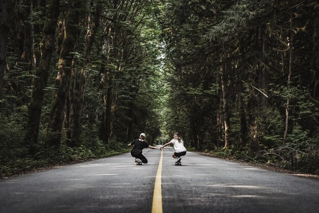 Bela foto de fêmeas de mãos dadas patinando em uma estrada vazia no meio da floresta