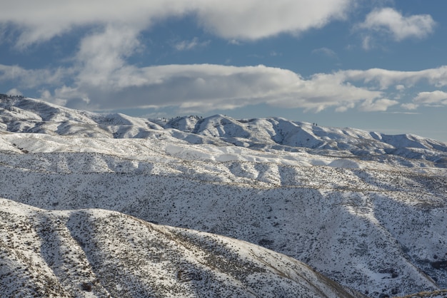 Bela foto de montanhas nevadas com árvores sob um céu azul nublado durante o dia