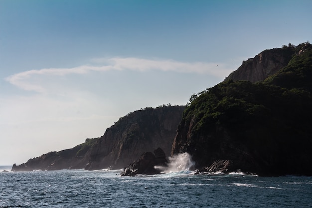 Foto grátis bela foto de ondas fortes do mar batendo em um penhasco com um céu azul