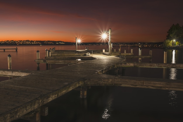 Bela foto de um cais de madeira iluminado no lago ao redor da cidade à noite