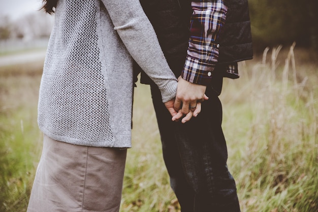 Bela foto de um casal se beijando, mantendo as mãos com um fundo desfocado