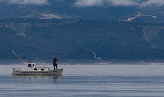 Bela foto de um homem em um barco, pegando peixes no lago com montanhas ao fundo