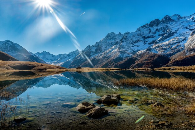 Bela foto de um lago cristalino ao lado de uma base de montanhas nevadas durante um dia ensolarado