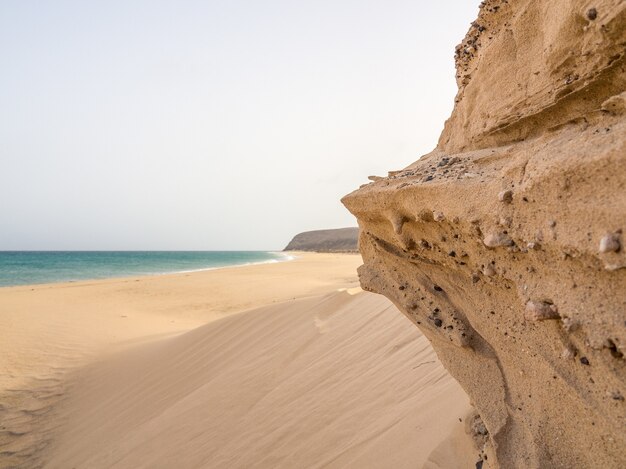 Bela foto de um litoral rochoso com areia fofa e mar azul em Fuerte Ventura, nas Ilhas Canárias