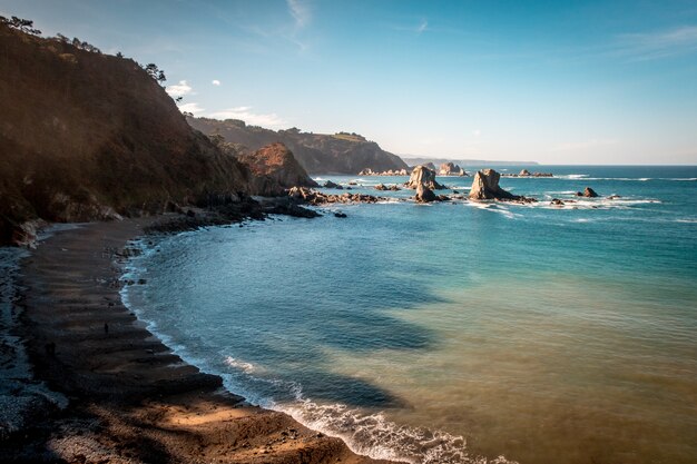 Bela foto de um mar calmo com colinas ao lado sob um céu azul em Asturies, Espanha