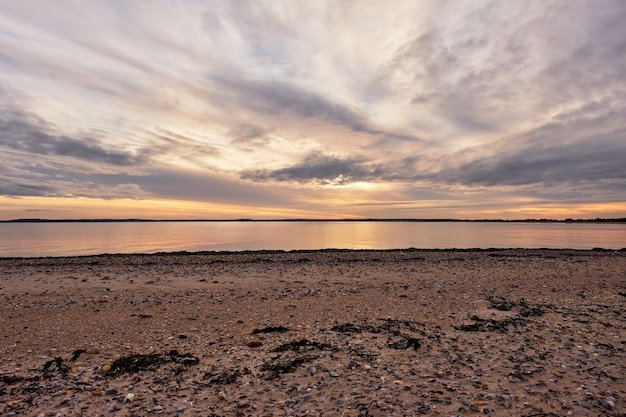 Bela foto de um oceano calmo com um cenário de pôr do sol em um céu azul nublado