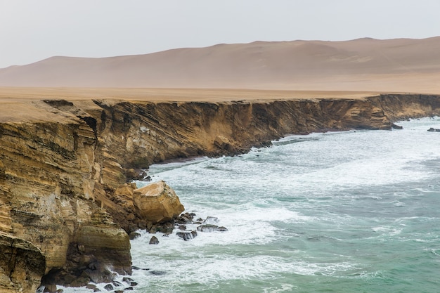 Bela foto de um penhasco perto do mar com montanhas ao longe